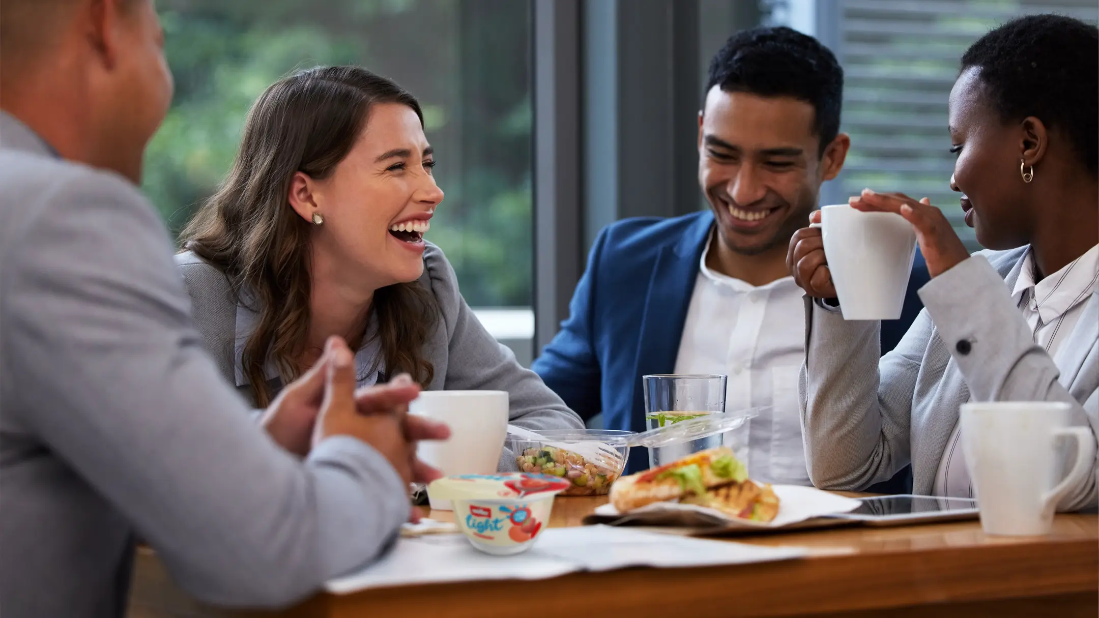 Group of friends sat at a table eating lunch with a MüllerLight yogurt pot on the table